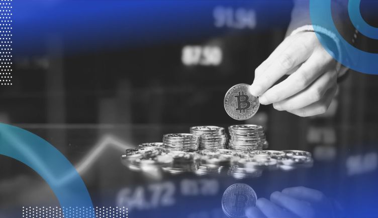 A hand adds a Bitcoin to a stack in front of market trend lines