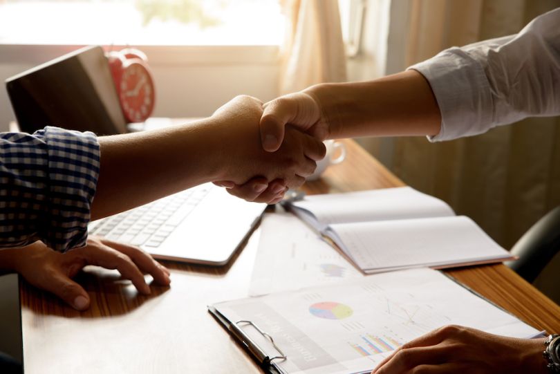 Two men shake hands at a desk