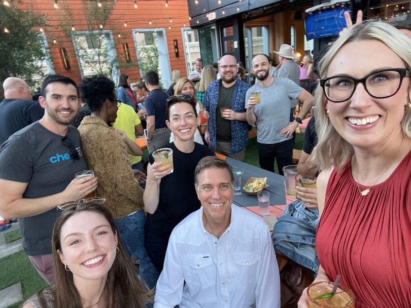 Group selfie shot taken outside at a dining area with picnic tables and string lights