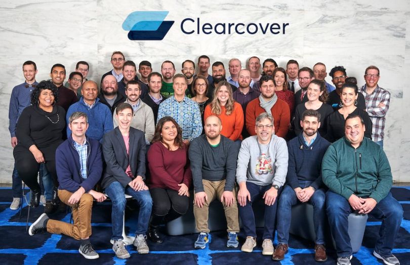 Clearcover team in office posing for photo below their logo