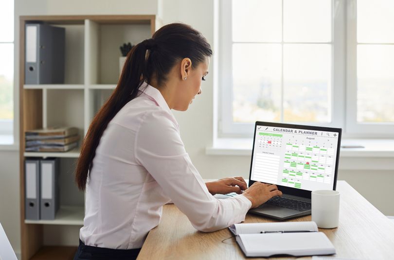 Busy female secretary at desk checks smart calendar