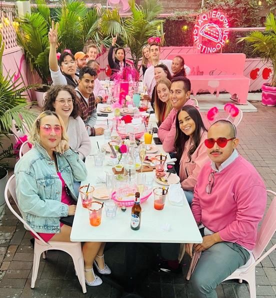team meal with people around a long white table and pink decor everywhere