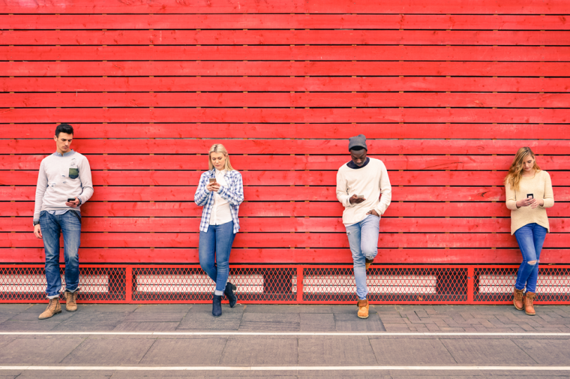 People Looking at Phones on Red Fence