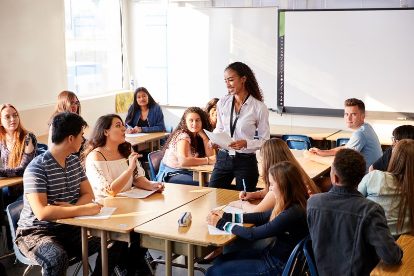 High School Teacher Standing By Student Table Teaching Lesson