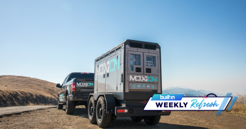 A truck pulling a trailer both with Moxion's logo on them.