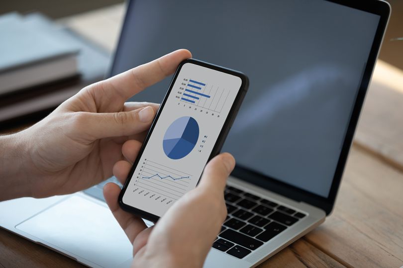 Close up businessman holding phone with graphs and diagrams on the screen