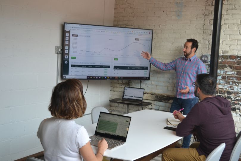 A team of analysts at ClearCut gather around a line graph of data to discuss strategy.