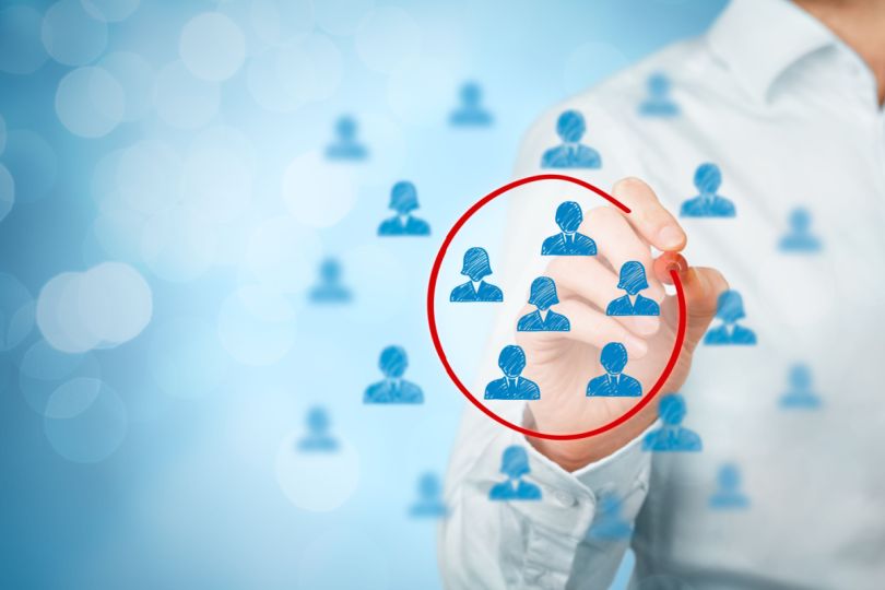 A marketing professional in business attire circles a selection of blue icons representing targeted consumers with a red marker. 