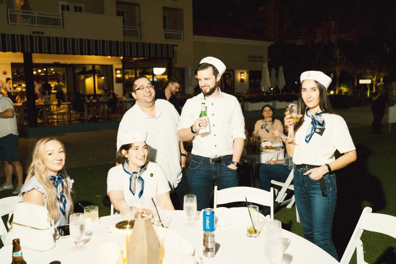 Excel team members pictured in sailor hats and white shirts at a team gathering, clustered around tables