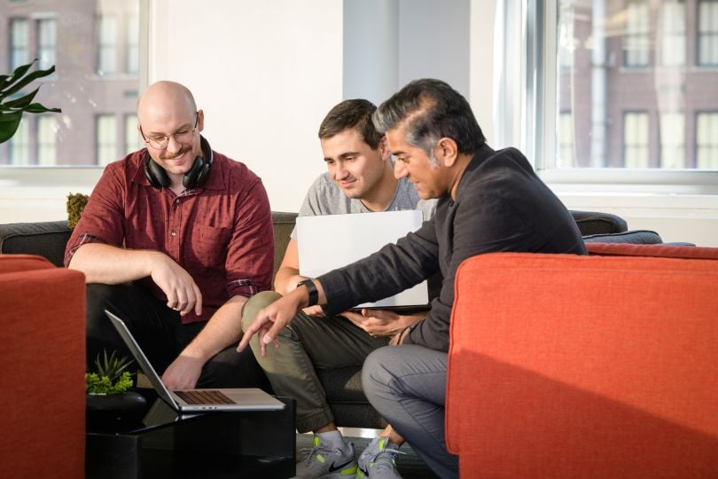 Three of Network Perception's employees seated in orange chairs, crowded around a laptop and discussing something.