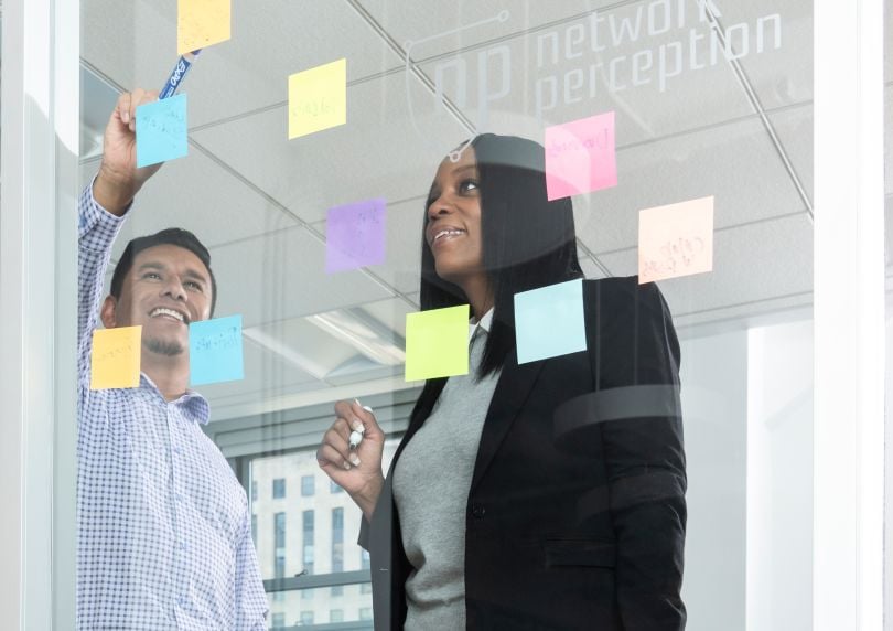 Shanita Pearson and another coworker looking at a pane of glass with post-its on it in collaboration. Both are smiling.