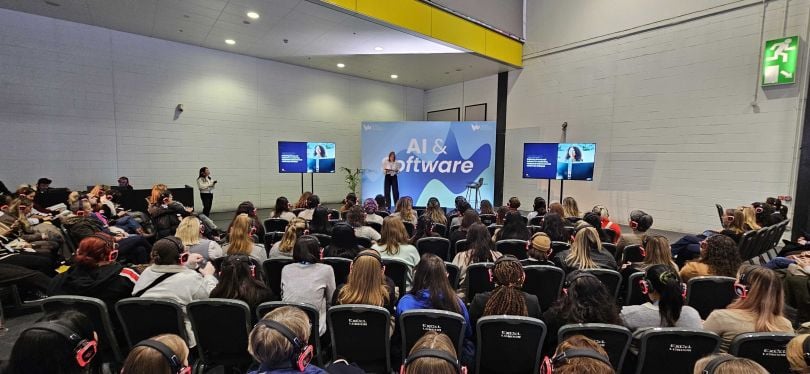 Event photo of GitLab leader standing on a stage in front of a seated audience, with a backdrop that reads “AI & Software.” 