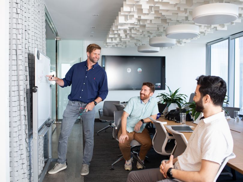 Solution Architect Cory Clark leads a team meeting while discussing ideas with two other teammates.