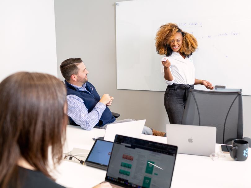 an employee at the whiteboard collaborating with two other employees at a table