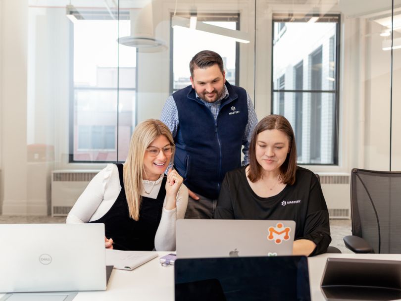 three employees in the office looking over a laptop