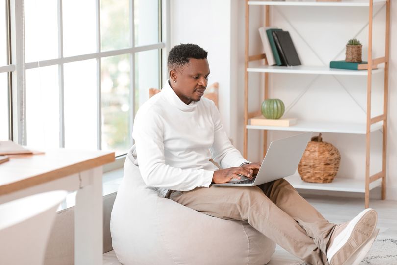 African-American man working on laptop at home sitting in a beanbag chair