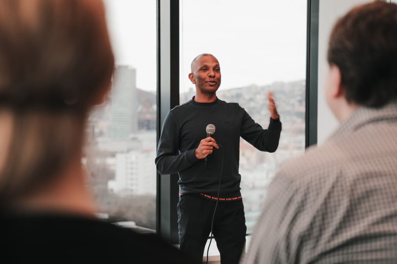 Candid photo of GoHealth CTO Jay Sreedharan speaking to a group of people with a microphone, gesturing with his hand