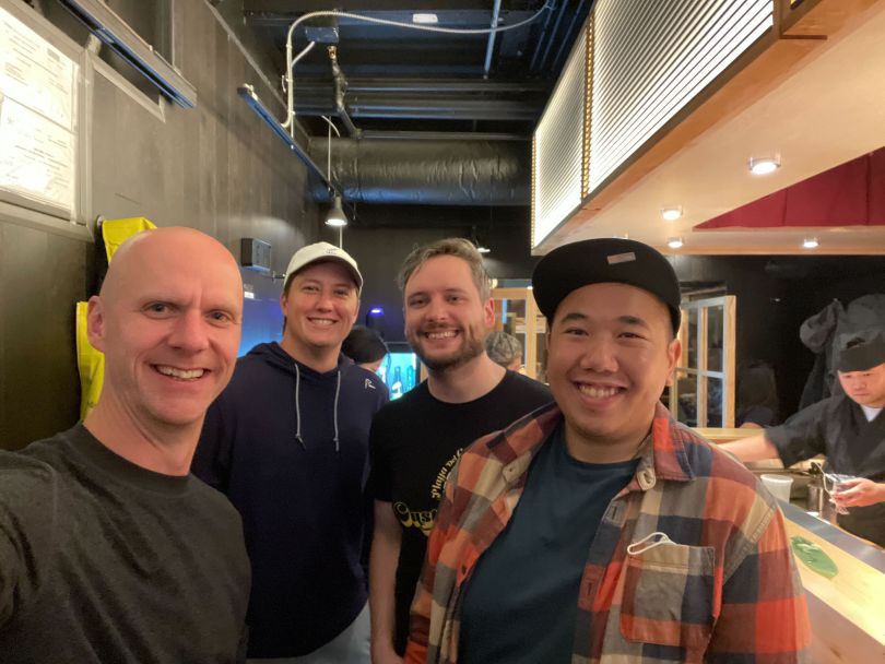 Four Customer.io colleagues smile at sushi counter