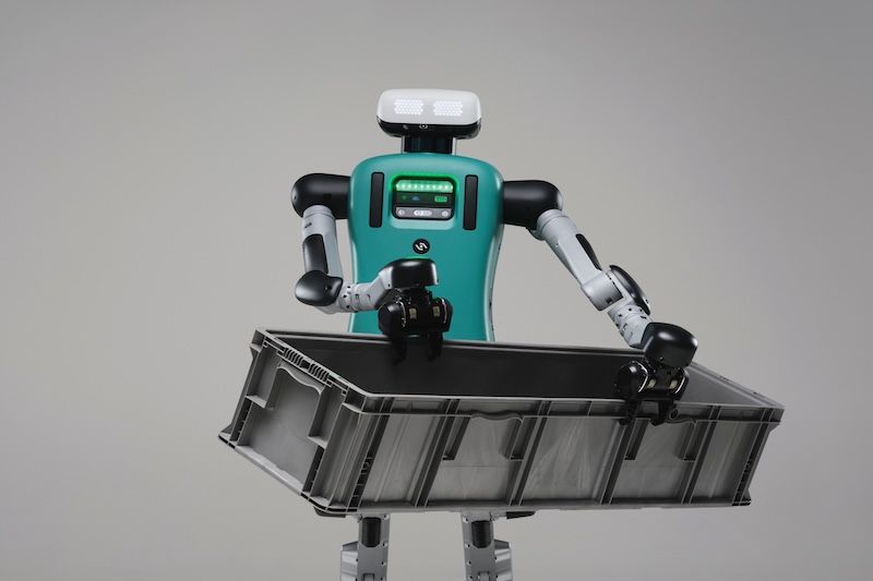 The humanoid robot, Digit, carrying a cardboard box in an office setting.