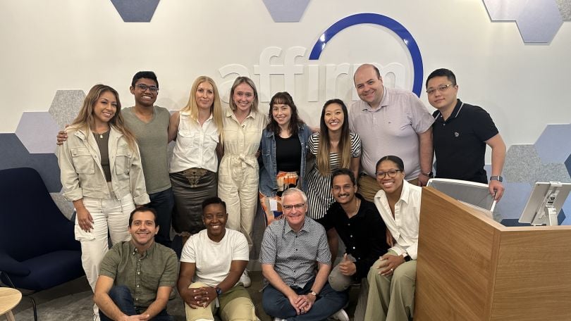 A group of Affirm team members pose for a photo in front of the company logo on a wall in the office.