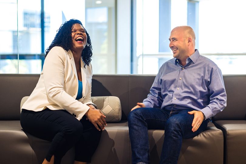 Alteryx coworkers sitting on a couch in the office smiling and laughing