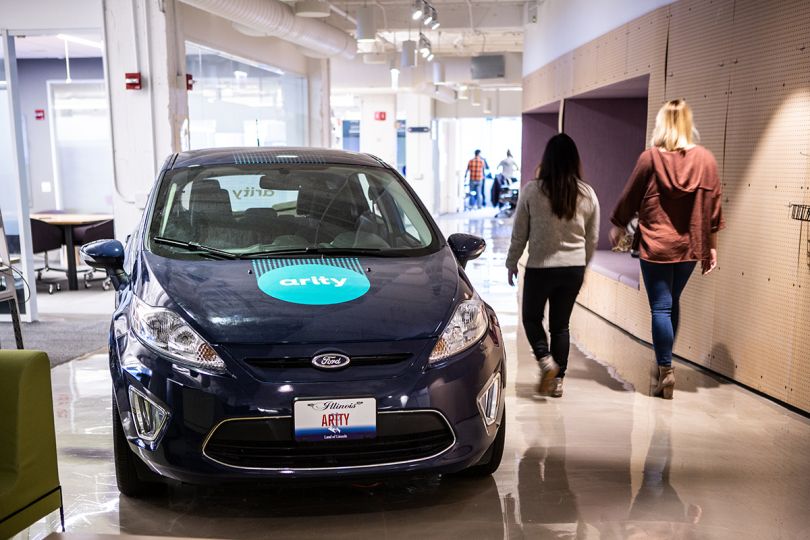 Team members walking by a car in the office with the Arity logo on it