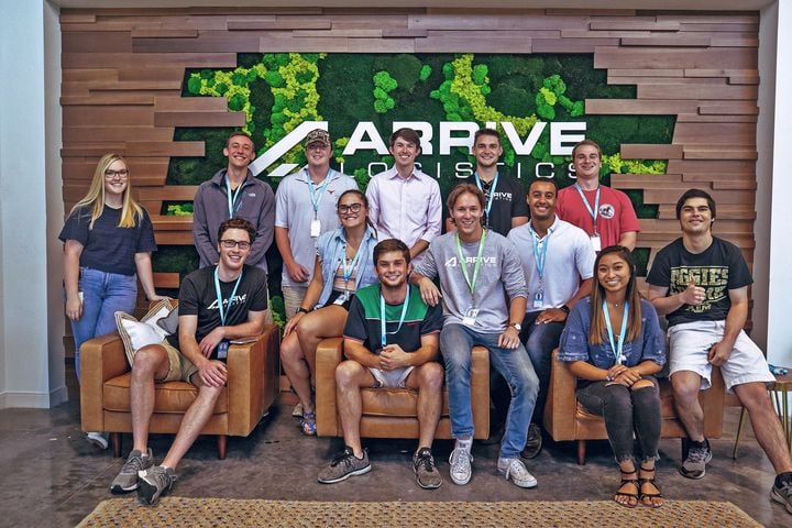 Arrive Logistics group photo in the office with the company logo on the wall behind them