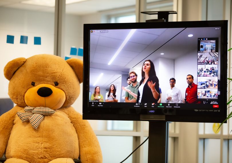 Virtual event woman speaking in a room of people on a screen that's next to a stuffed bear