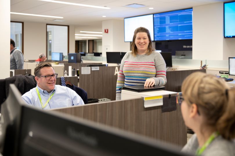 Candid photo of three OCC colleagues talking at their desks