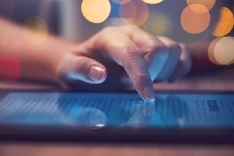 A hand scrolls through news on a tablet