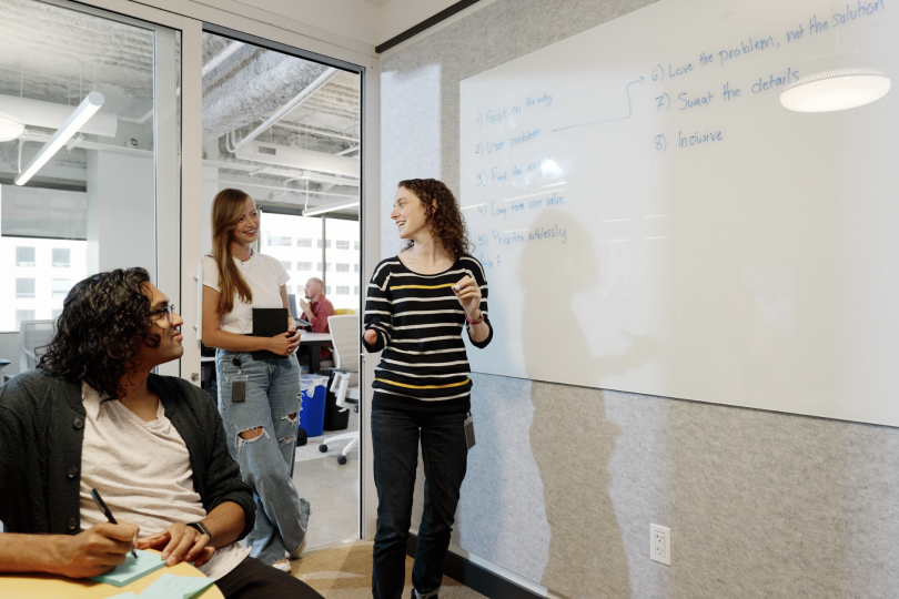 Three people are collaborating in a conference room with a whiteboard