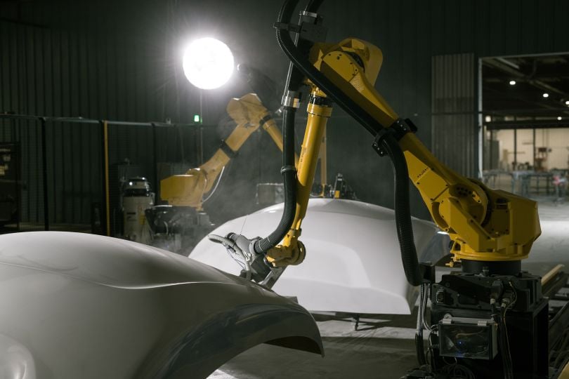 A yellow robotic machine crane makes a white plastic object. 