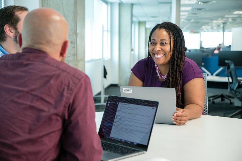 Woman with laptop sitting at table smiling at two people across from her