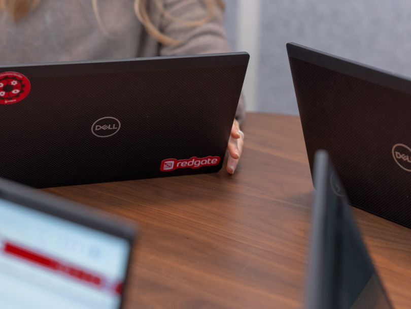 Tech workers sit around a conference table; a close up displays a Redgate logo on one of their laptops