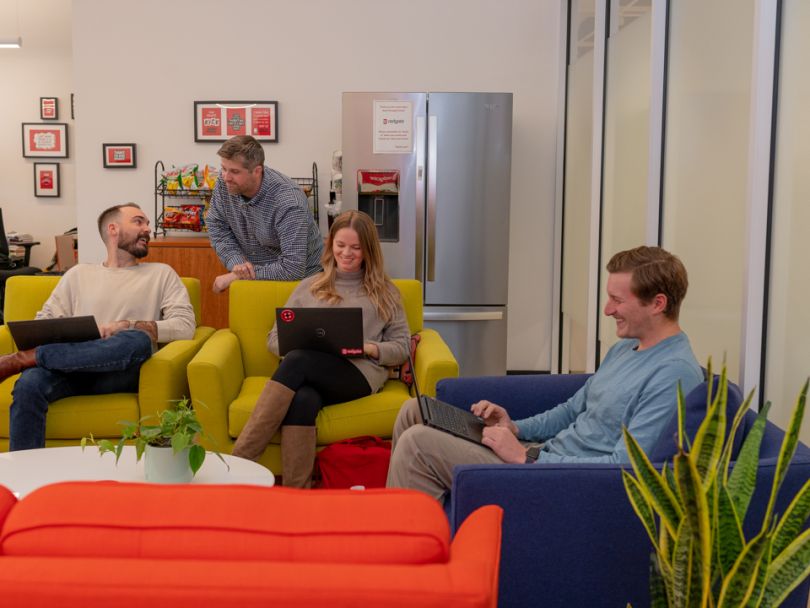 four employees in lounge area working on colored couches