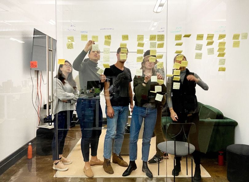 A small team organizes yellow post-its on a glass wall