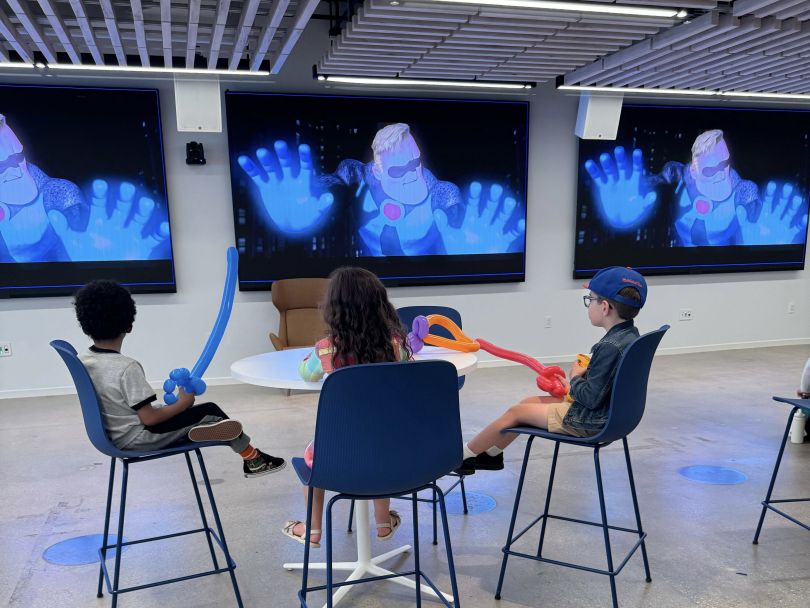 Children sit with balloon animals and watch The Incredibles during Braze’s Take Your Kids to Work Day celebrations.