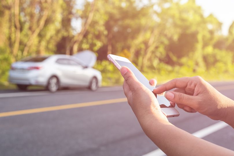 Close up hand of woman using smartphone and blur of her broken car parking on the road.