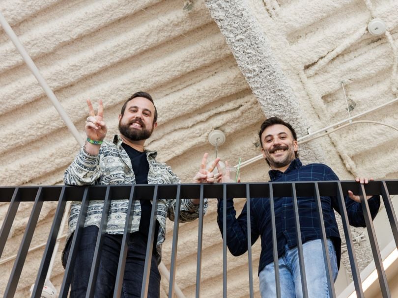 Two CarGurus sales representatives smile and share peace signs as they look down from a floor above.