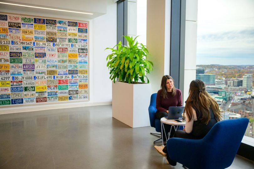 Two women sit across from each other at a table near a large window at CarGurus office&nbsp;