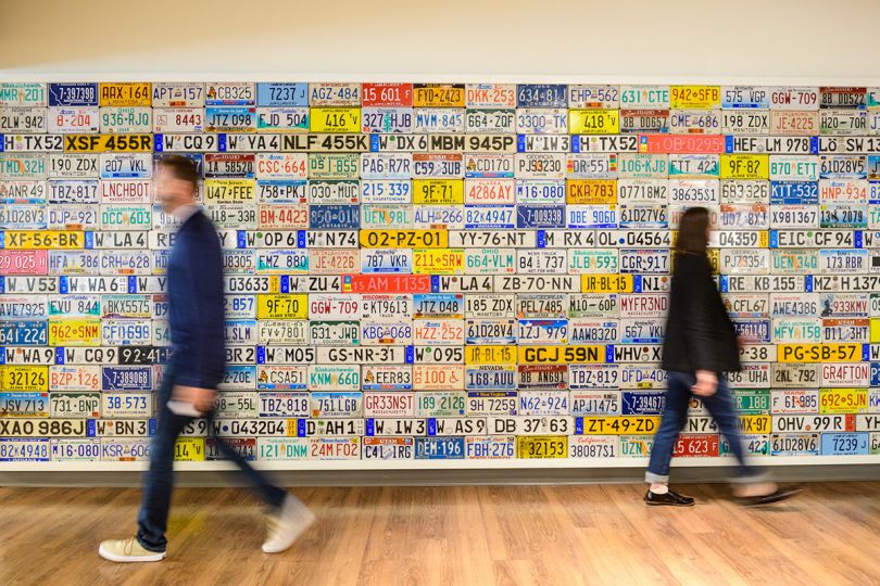 CarGurus team members walking past a wall of license plates in the office