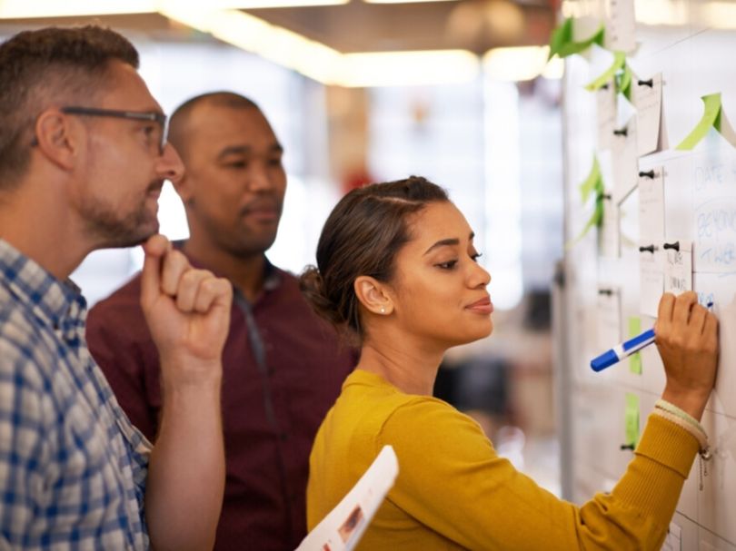 Employees brainstorming ideas together using sticky notes on a whiteboard