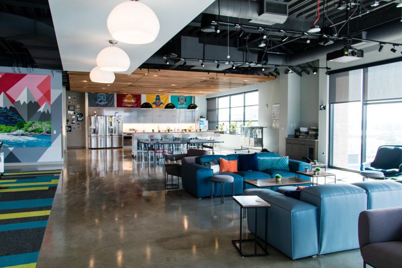 A photo of Choozle's office living room featuring modular blue sofas and looking toward the kitchen with a large island and flags hanging over the counter