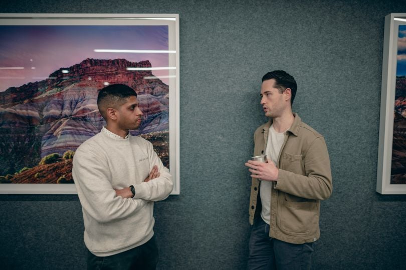 Two co-workers facing each other talking against a wall in Range's office