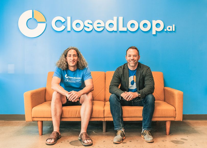 Closedloop team members sitting on a couch with the Closedloop logo on the wall behind them