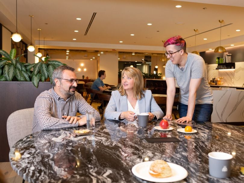 Erhan Musaoglu and Elizabeth Walsh site at a table with coffee, talking to a team member.