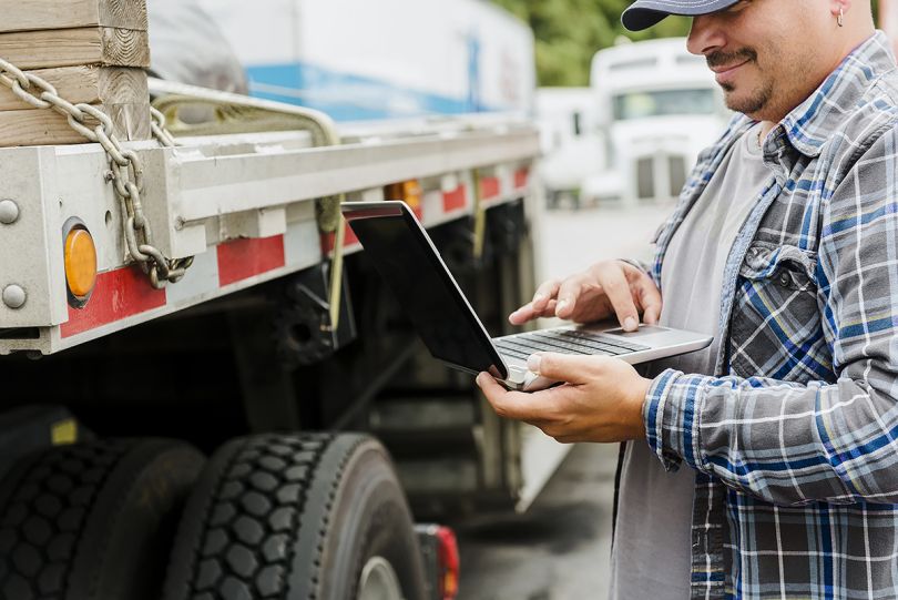 DAT driver standing outside of truck looking at a laptop