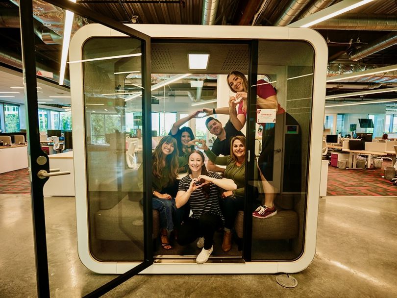 Photo of Restaurant365 team members piled into an office meeting pod, making hearts with their hands.