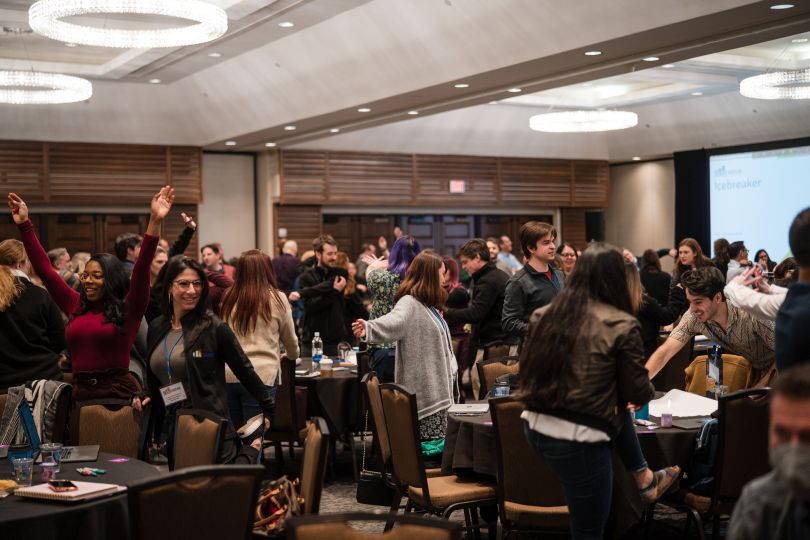 Conference room of people getting up from tables to stretch, smiling.