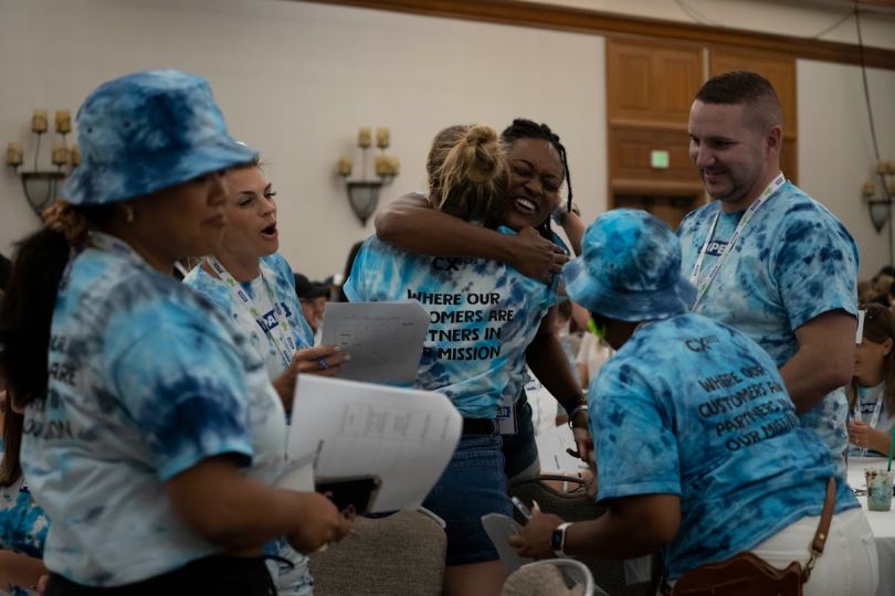 Candid photo of Team members in tie-dyed T-shirts hugging at event